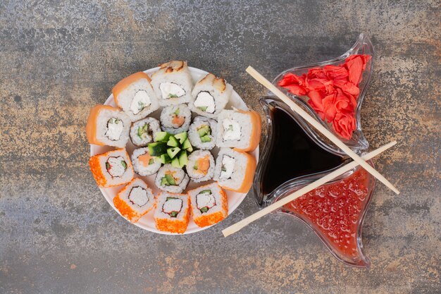 Set of delicious sushi with chopsticks and ginger on marble surface