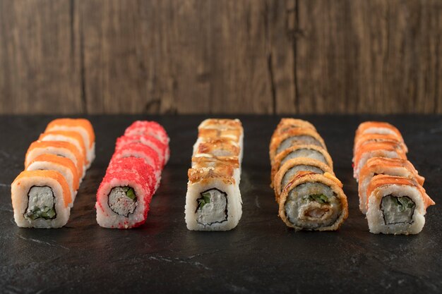 Set of delicious traditional sushi rolls on black surface