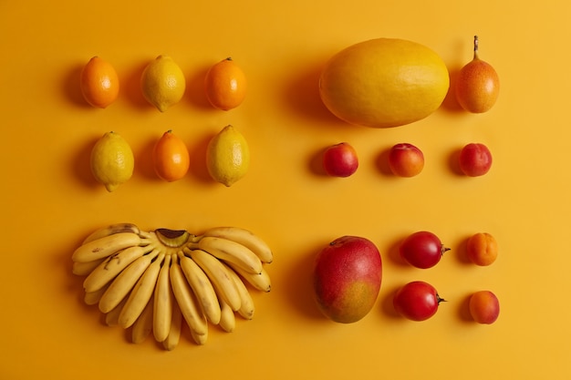 Free photo set of delicious tropical fruits for consumption. lemons, cumquat, peaches, tamarillo, bananas, melon on yellow background. nutritious crops rich in vitamins used as ingredients for fruit salad