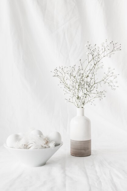 Set of Easter eggs and quills in bowl near plant branches in vase