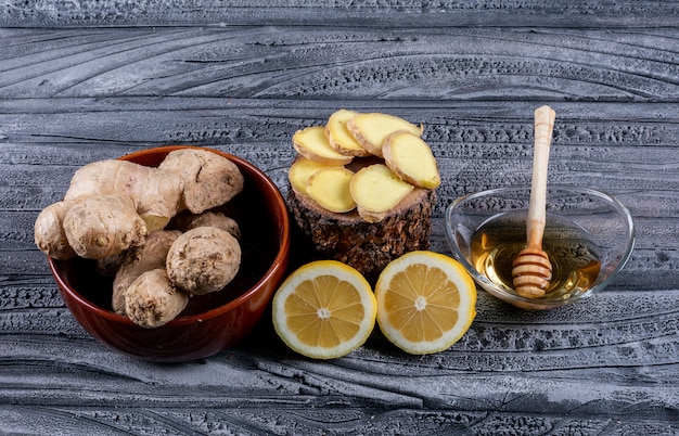 Free photo set of ginger slices, lemon and ginger and honey in a bowls on a dark wooden background. top view.