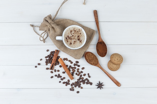 Free photo set of grinded coffee, spices, coffee beans, cookies and coffee in a cup on wooden and sack background. top view.