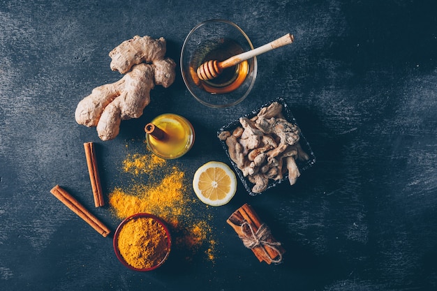 Free Photo set of honey, lemon, ginger and dry cinnamon pack and ginger powder in bowls on a dark textured background. top view.