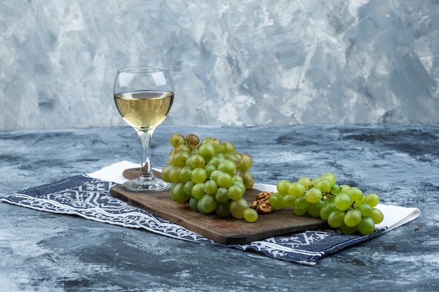 Set of kitchen towel, glass of whisky and white grapes on a cutting board on a dark and light blue marble background. close-up.