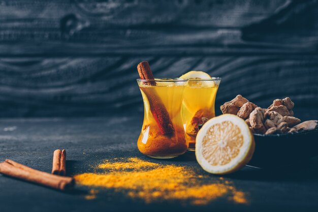 Set of lemon, ginger and dry cinnamon and ginger powder in a tea cups on a dark textured background. side view. space for text