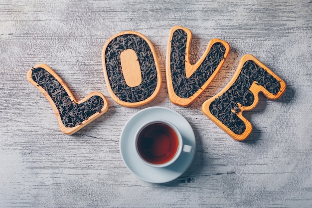 Free photo set of love text filled with tea and a cup of tea on a white wooden background. top view.