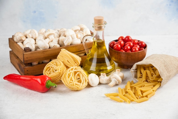 Set of mushrooms, extra virgin olive oil, pastas, cherry tomatoes and chili peppers on a piece of marble.