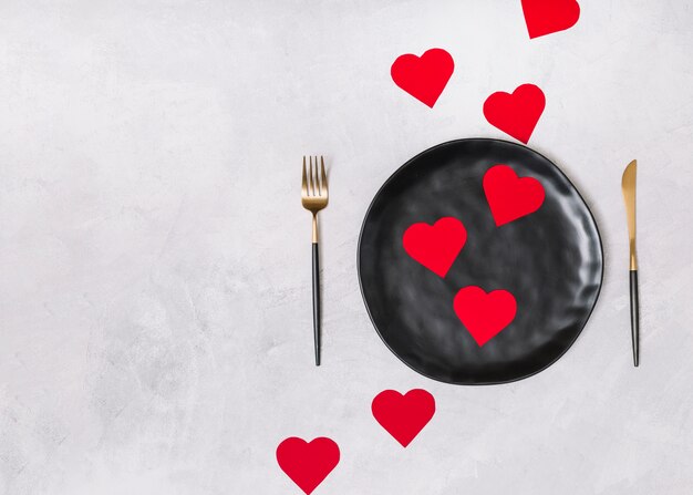 Set of ornament hearts on black plate between cutlery