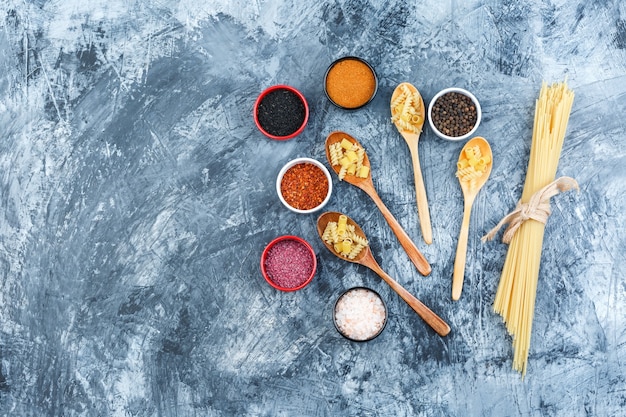 Set of spices and raw pasta in wooden spoons on a grey plaster background. top view.