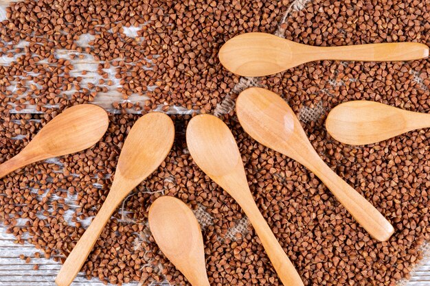 Set of spoons on top and buckwheats on a white wooden background. top view.