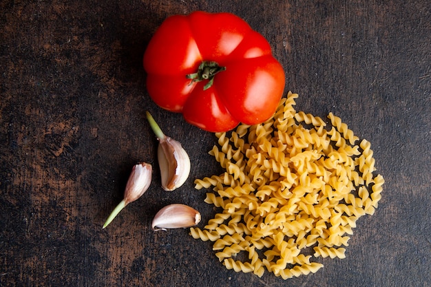 Set of tomato and garlic and macaroni on a dark textured background. top view.