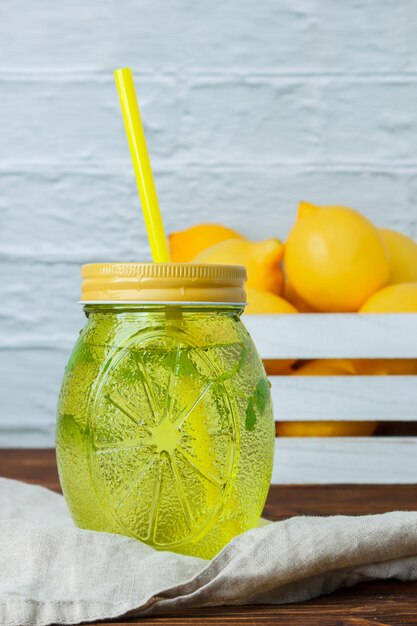 Free photo set of white cloth, lemons on wooden crate and lemon juice jar on a wooden and white surface. side view. space for text