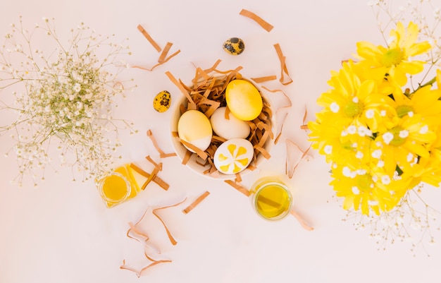 Free photo set of yellow easter eggs in bowl between fresh flowers and cans of colorant liquid