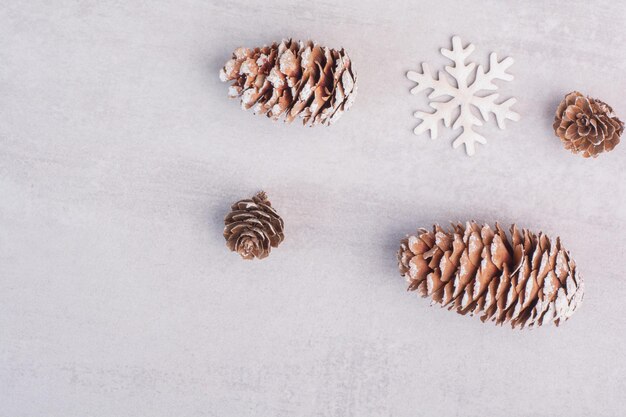 Several pine cones and snowflakes on white table.