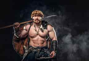 Free photo severe barbarian in warrior clothes, posing on a dark background.