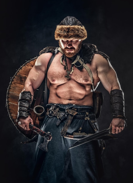 Free photo severe barbarian in warrior clothes, posing on a dark background.