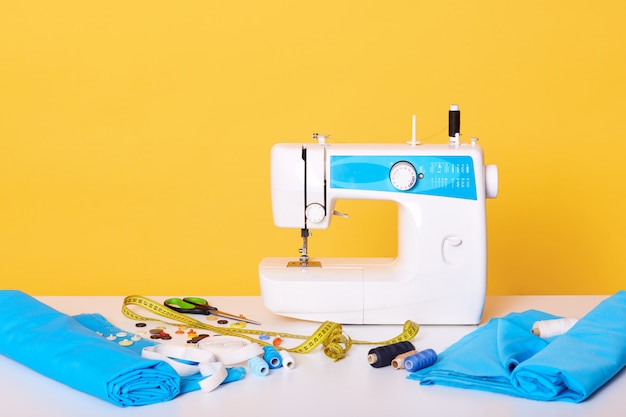 Free photo sewing equipments, sewing machine, tap measure, scissors, pieces of cloth, needles, thread isolated on yellow. different tools in sewing workshop,