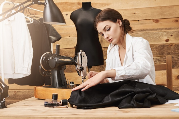 Sewing is not just work, it is flair. Creative designer working with sewing machine under her new garment line, being focused and putting efforts to make it look great while being in her own workshop