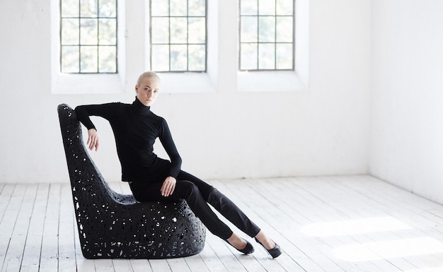 Free Photo sexy blond female in a black costume sits on a round black chair in  empty room.