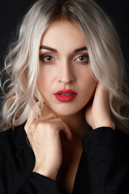 Sexy blonde with long curly hair poses in black jacket in a dark studio