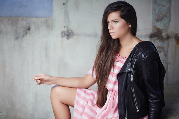 Sexy brunette in pink dress and leather jacket posing on camera.