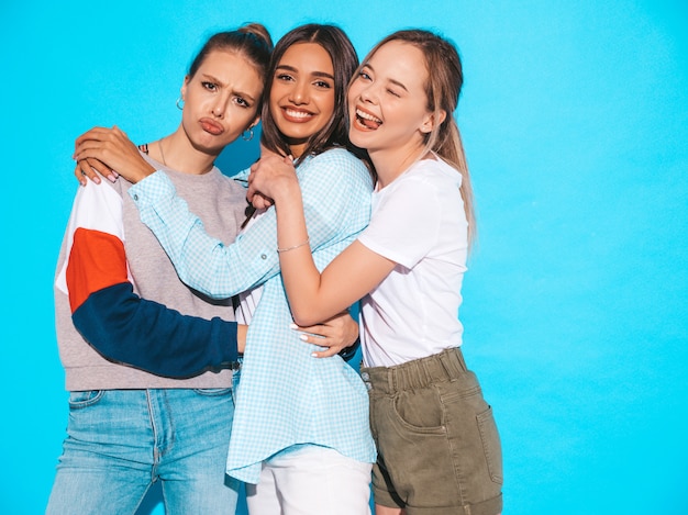 Free photo sexy carefree women posing near blue wall in studio. positive models having fun and hugging