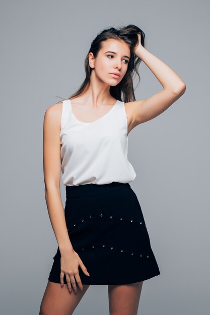 Sexy girl in fashion modern dress is posing in studio holds her arms on hair isolated on white background