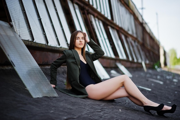 Sexy model girl wit long legs at black lingerie outfit body swimsuit combidress and jacket posed at the roof of abadoned industrial place with windows