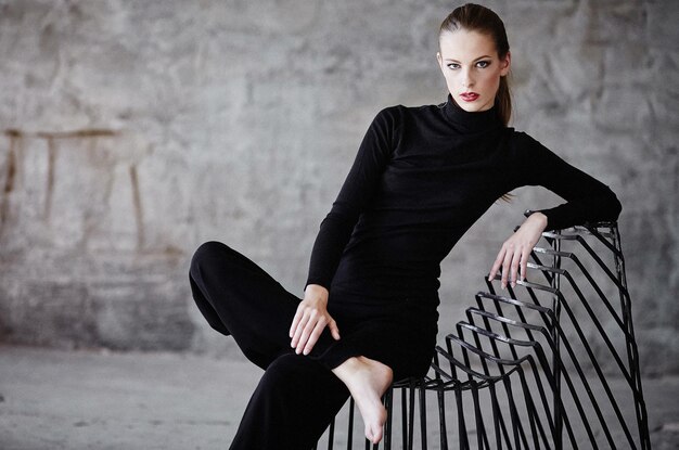 Sexy woman in a black clothes sitting on a chair.