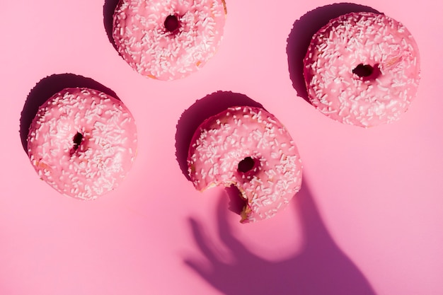 Shadow of a person's hand near the eaten donuts against pink background