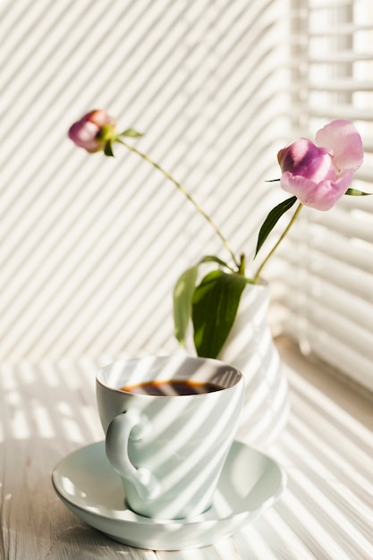 Shadow of window blinds on coffee cup and flower vase