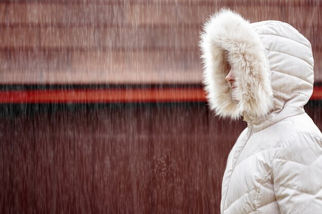 Shallow focus of an adult female wearing a white winter coat and walking under the snow