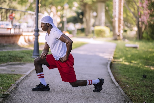 Shallow focus shot of an African-American male in a white shirt stretching at the park