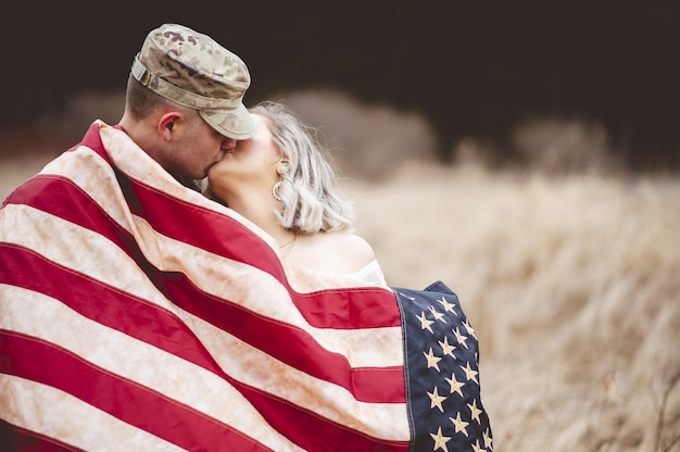 Shallow focus shot of an American soldier kissing his loving wife while wrapped in an American flag