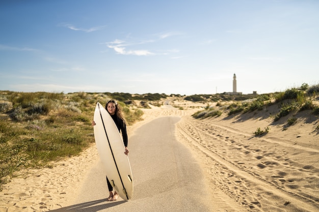 Free photo shallow focus shot of an attractive female holding a surfboard in the middle of the road in spain