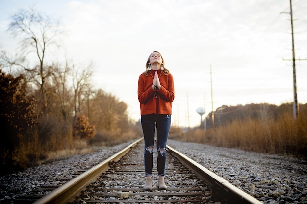 Shallow focus shot of a female standing on train tracks while praying