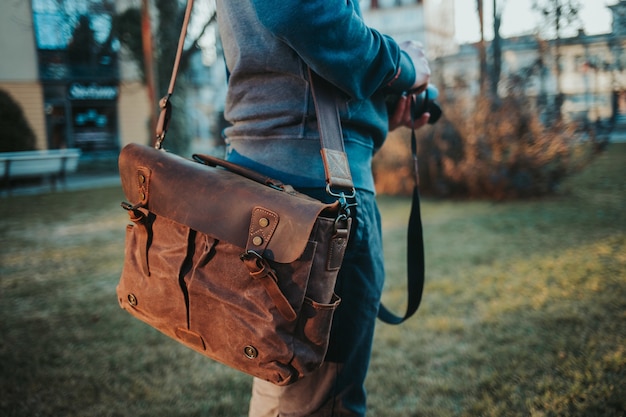 Shallow focus shot of a male wearing a brown leather satchel and holding a camera