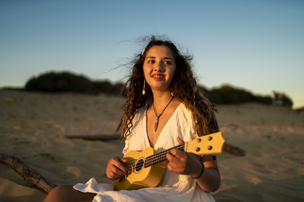 Free photo shallow focus shot of a smiling female playing a yellow ukulele at the beach