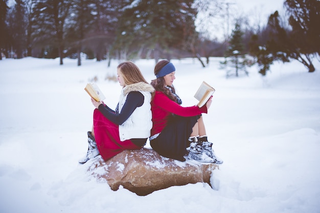 Free Photo shallow focus shot of two female sitting on the rock back to back while reading the bible