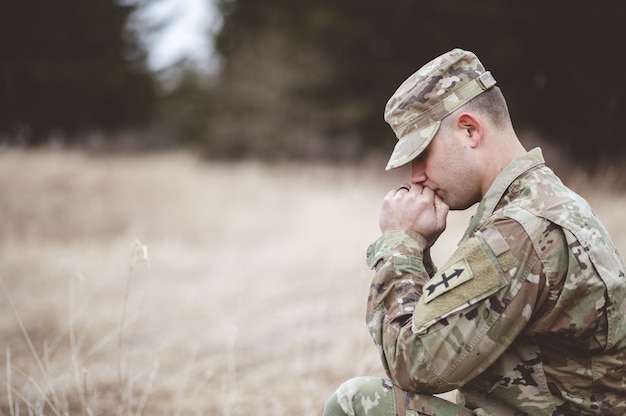 Free photo shallow focus shot of a young soldier praying in a field