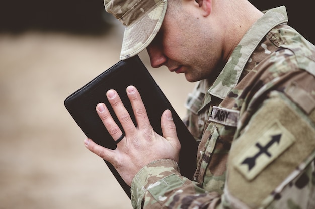 Free photo shallow focus shot of a young soldier praying while holding the bible