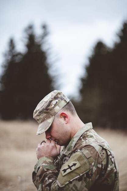 Free photo shallow focus vertical shot of a young soldier praying in a field