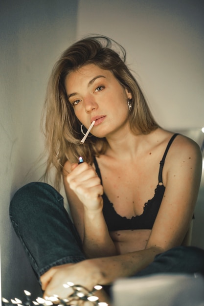 Shallow focus of a woman lighting a cigarette on her bed with light garlands behind