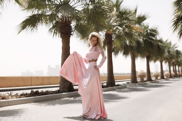 Free photo shapely blonde next to the sea in dubai, palm trees, hot, gorgeous dresses, summer sunny lifestyle fashion shooting, waving in the wind dress, calm and chilling out near the pool, hairstyle, makeup