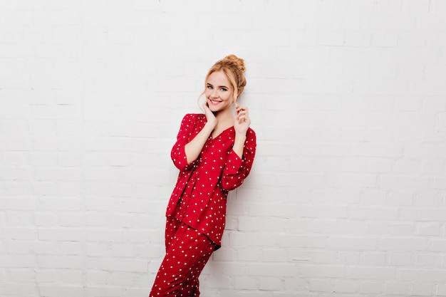 Free photo shapely caucasian girl in red sleepwear playing with her hair. laughing lady in cozy night-suit expressing true positive emotions.