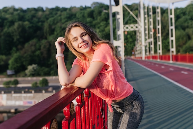 Free Photo shapely lady in sport uniform posing near cinder track. interested blonde girl chilling at stadium in morning.