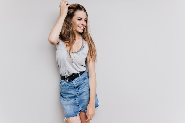 Shapely stunning girl playing with long dark hair. Indoor photo of adorable caucasian female model in trendy denim skirt.