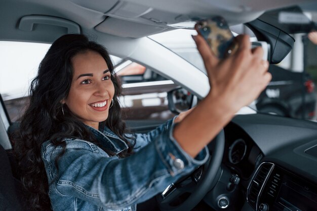 Sharing the happiness. Cute girl with black hair trying her brand new expensive car in the automobile salon