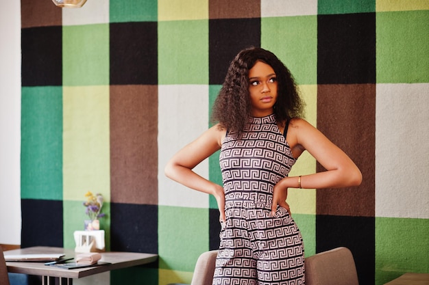 Free Photo sharming elegant young african american woman with long curly hair wearing jumpsuit posing at cafe indoor