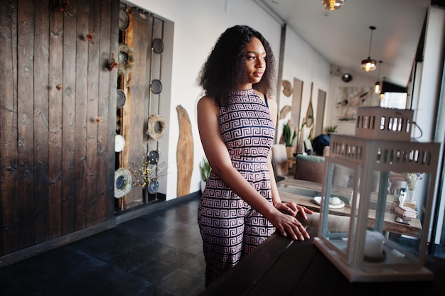 Sharming elegant young african american woman with long curly hair wearing jumpsuit posing at cafe indoor